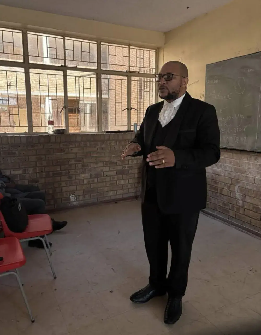 A speaker in advocate's court dress addressing learners in a classroom