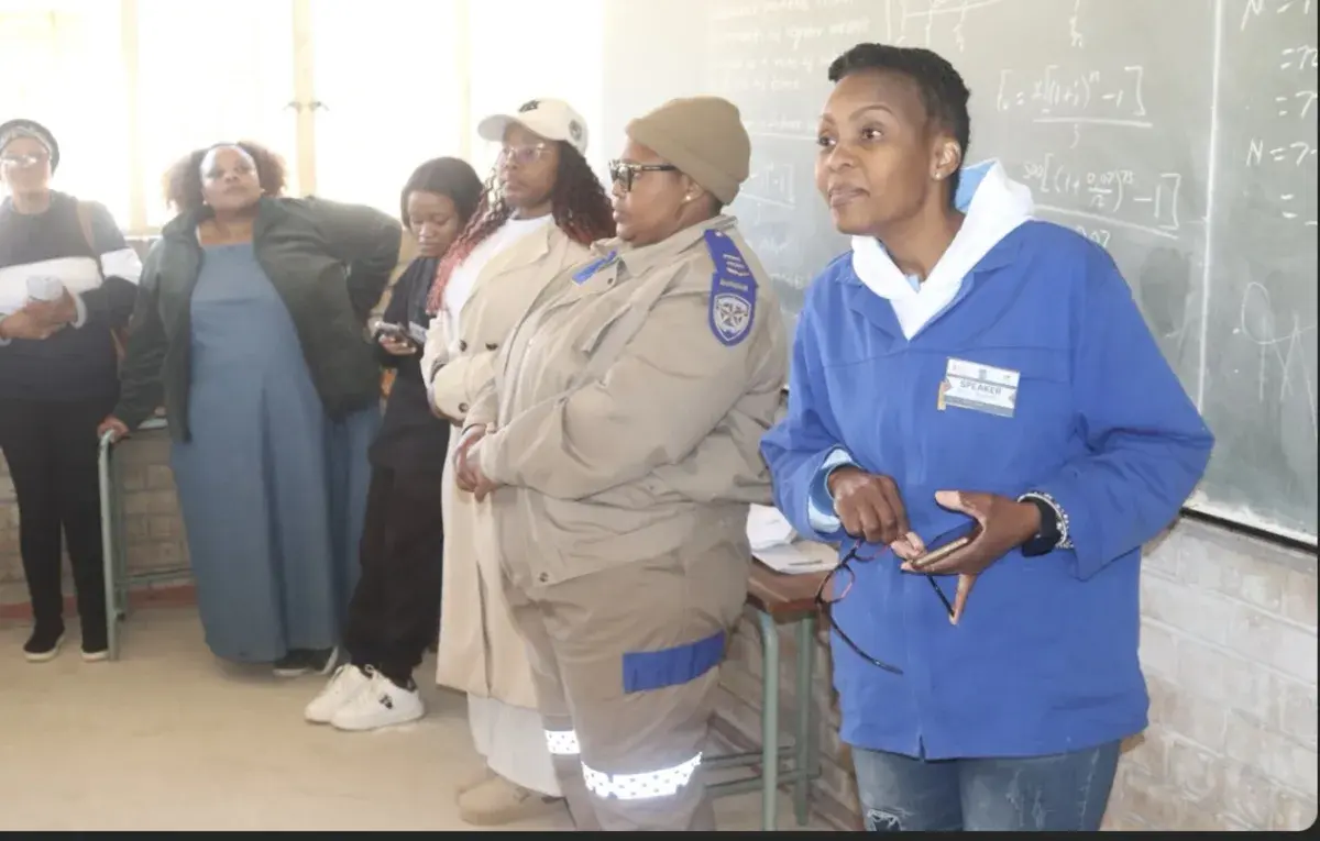 A speaker in a blue jacket addressing learners, with other speakers looking on